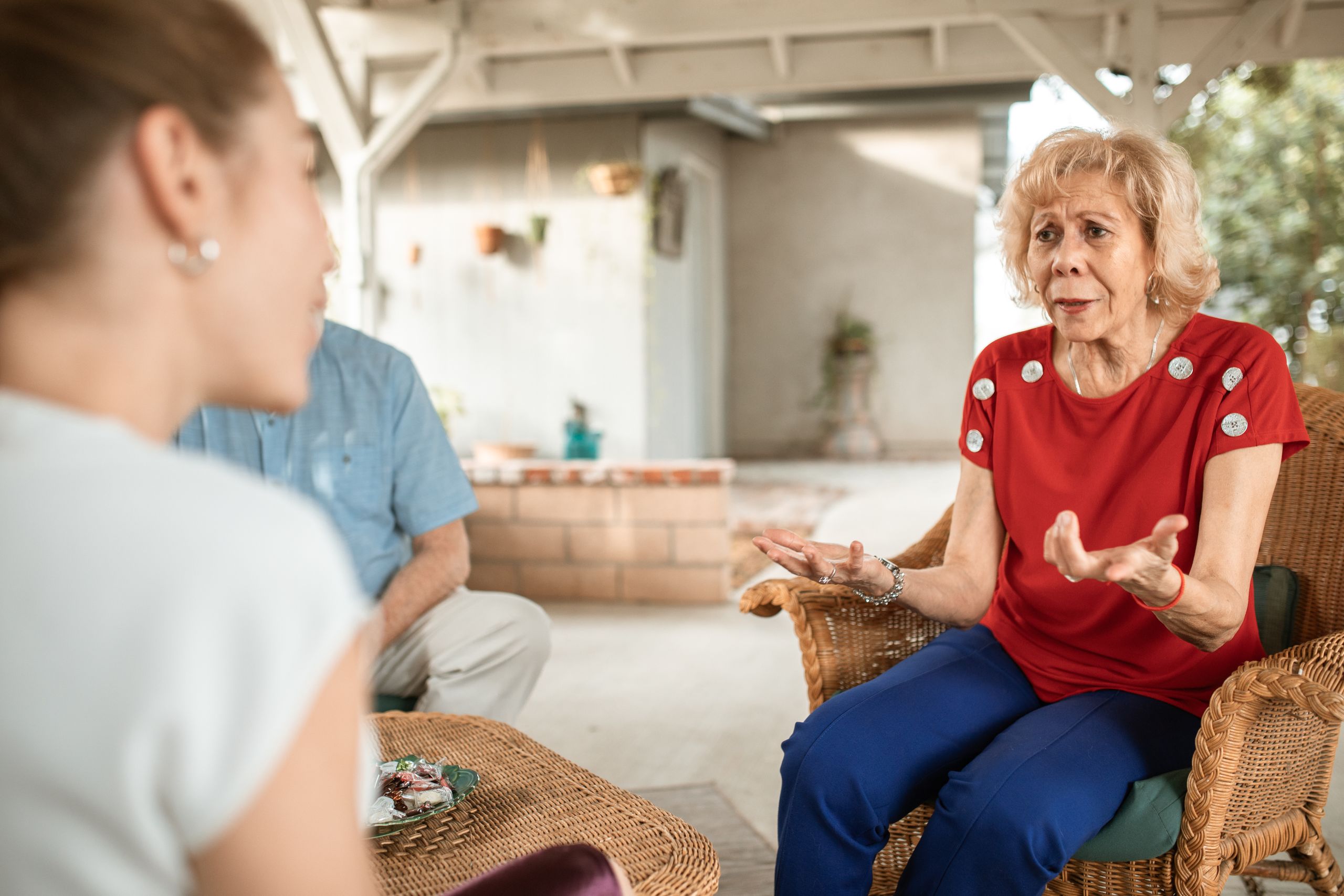Senior woman in a red shirt chatting expressively with another woman in a cozy setting.